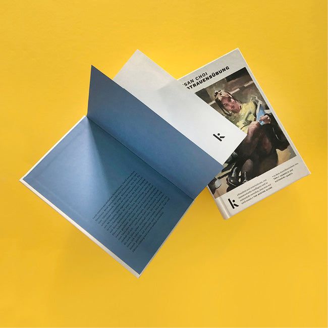 Foto von »Vertrauensübung«, links aufgeschlagen mit Klappentext, rechts dahinter das Cover.