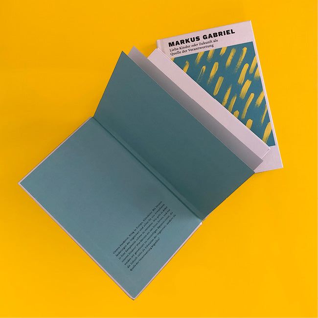 Foto von »Liebe Kinder oder die Zukunft als Quelle der Verantwortung«, ein Buch aufgeschlagen mit dem Klappentext, eins mit der Vorderseite daneben.