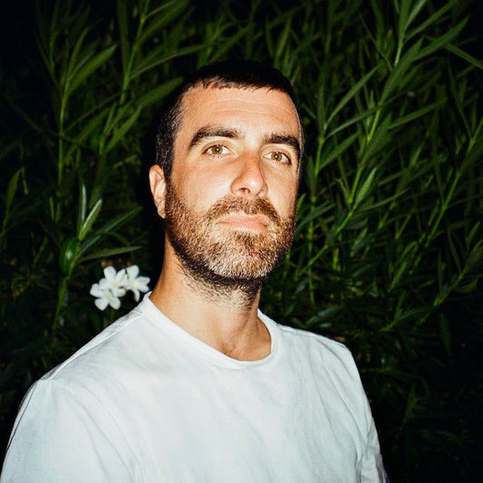 Porträt eines Mannes mit Bart und weißem Shirt vor grüner Pflanzenkulisse. Möglicherweise der Autor Davide Coppo, bekannt für seinen Roman »Der Morgen gehört uns«.
