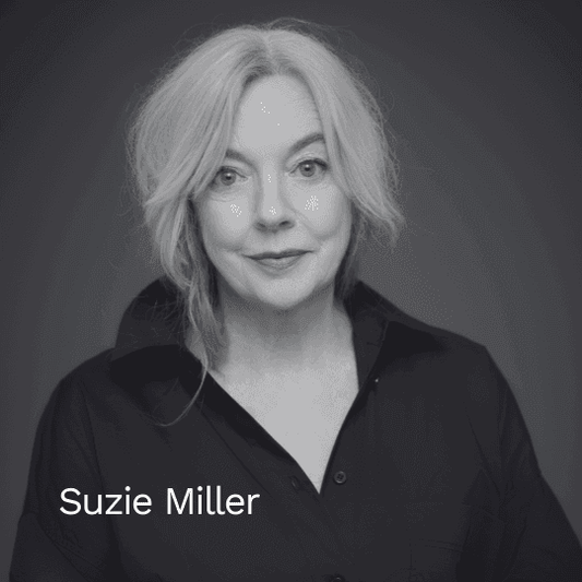 Schwarz-weiß Porträt der Autorin Suzie Miller vor einem dunklen Hintergrund. Sie blickt freundlich in die Kamera und trägt ein dunkles Hemd mit offenem Kragen.