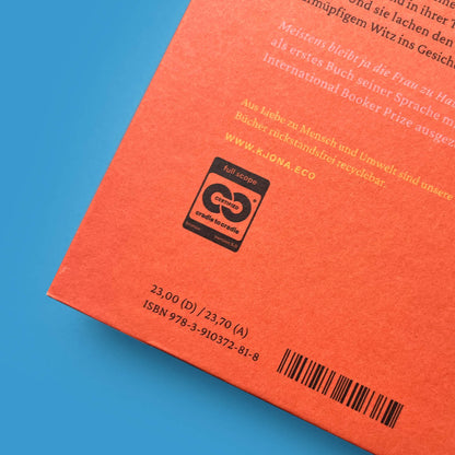 Nahaufnahme der Rückseite des Buchs von Banu Mushtaq mit Klappentext-Ausschnitt, Cradle to Cradle-Siegel und ISBN-Barcode auf orangefarbenem Grund.