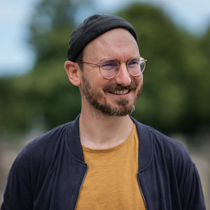 Wenn du hier nicht das Porträt von Lars siehst, dann läuft etwa schief. Der "junge" Mann sollte ansonsten mit seiner schicken Mütze vor einem verschwommenen Wald stehen. Haben wir irgendwann 2021 an der Isar fotografiert. Wir heißt in dem Fall Nina Rühr von SINN MEDIA. 🥳