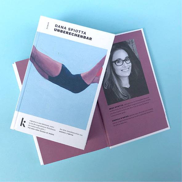 Foto von »Unberechenbar«, aufgeschlagen mit Autorinnenfoto im Hintergrund, Cover im Vordergrund. 