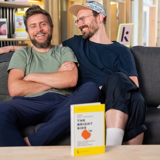 Lars stellt im Video auf einer Couch sitzend die Optimismus Kampagne kurz vor und bittet um Unterstützung. Er hält das Buch The Bright Side in den Händen.
